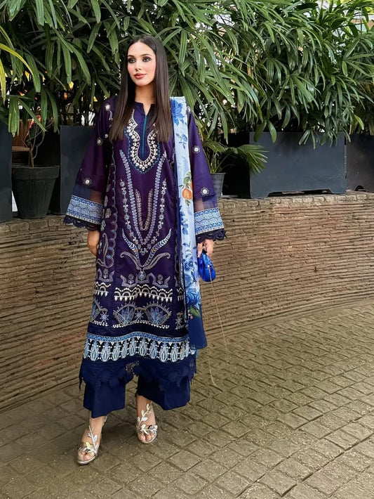 Woman in a blue and purple traditional outfit standing outdoors with greenery in the background